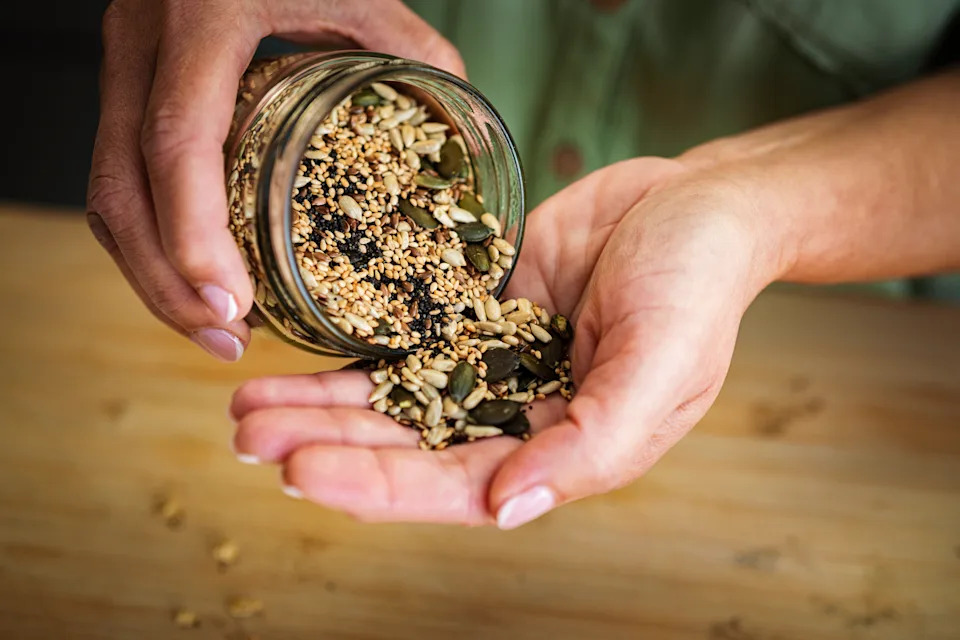 Woman scattering mixed seed on palm of hand from the jar