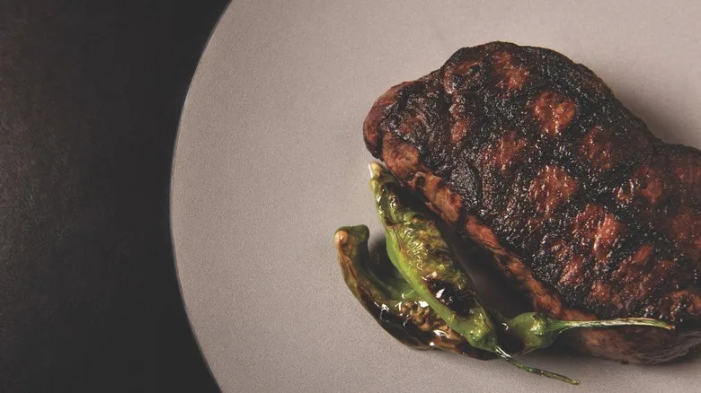 Grilled Wagyu ribeye on plate with shishito peppers