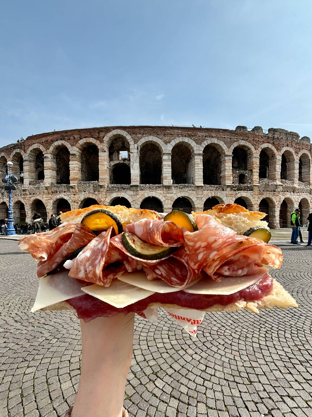 a hefty sandwich being held up in front of the Arena di Verona