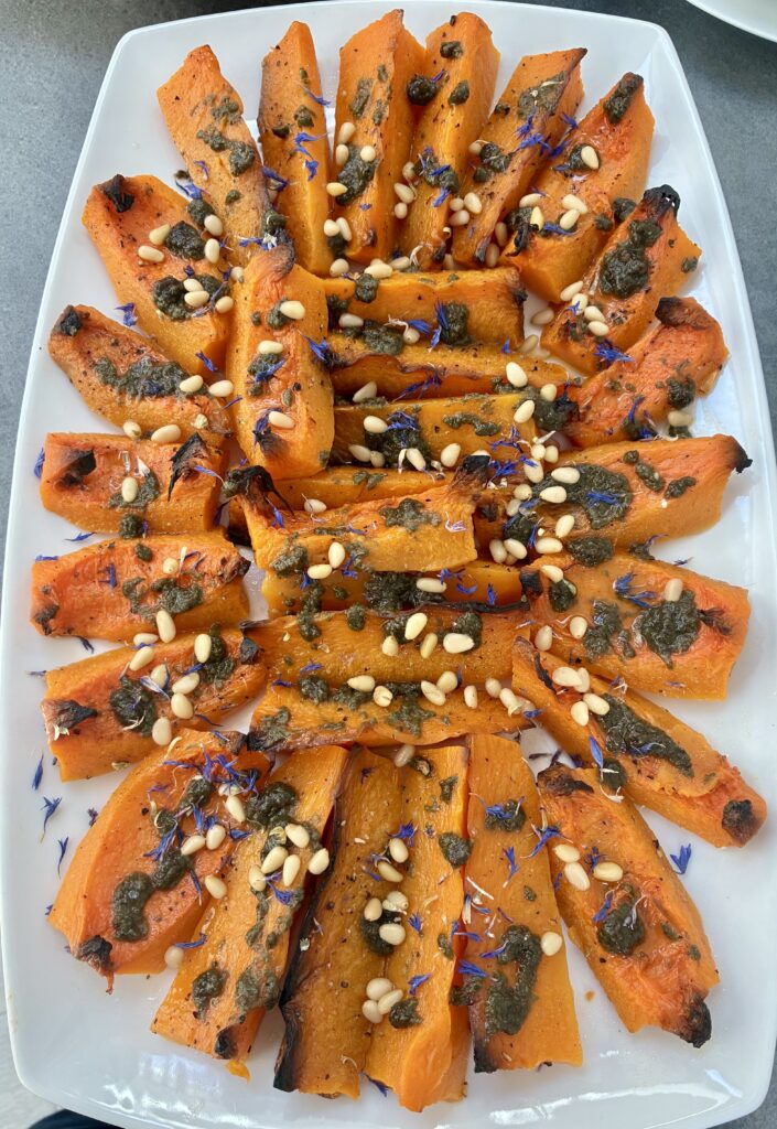 Roasted butternut squash wedges drizzled with a caper-raisin relish and pine nuts