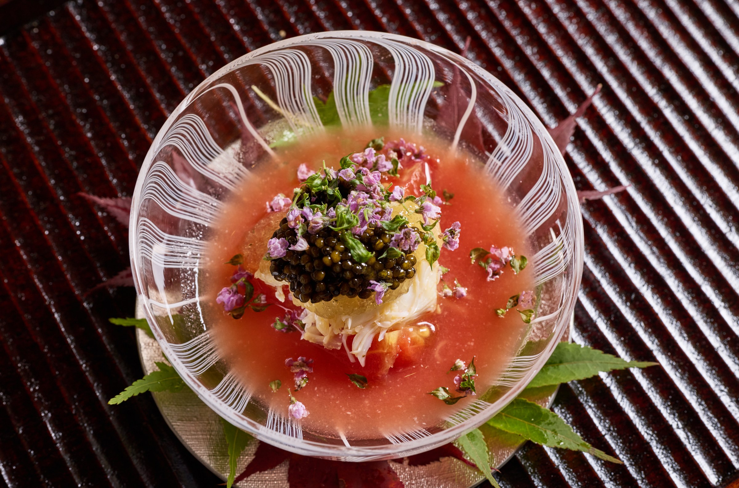 A bowl of red broth and white crab meat and caviar.
