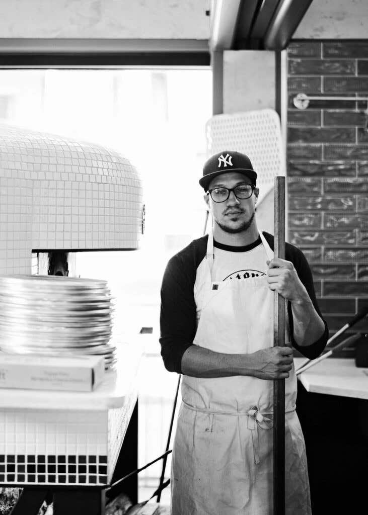 Chef Kyle Jacovino standing beside a pizza oven