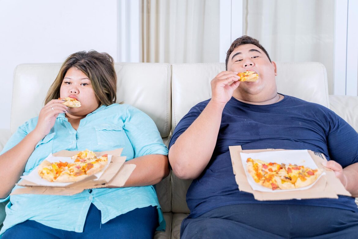 Obese Couple Eating Pizza on Sofa