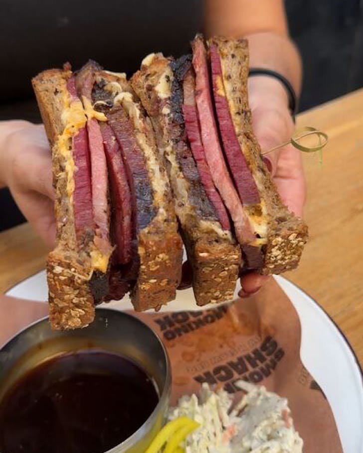 A stacked reuben sandwich and a pot of dipping sauce. 