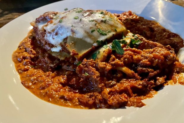 A plate of lasagna with a lot of Bolognese sauce on the plate