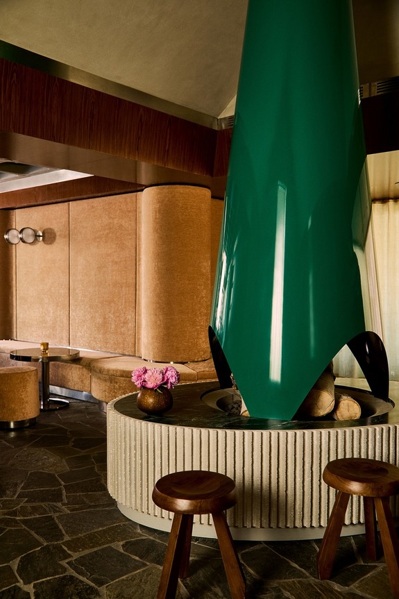 Modern interior with a green angular fireplace, wooden stools, and a cozy seating area in a room with stone flooring.