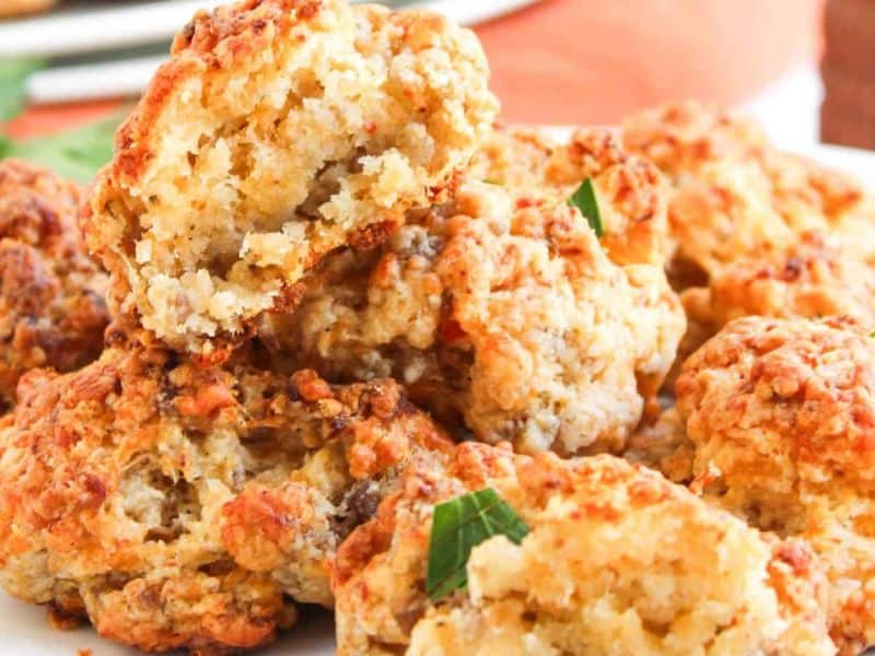 A plate of golden-brown, crumbly sausage and cheese biscuits, one with a bite taken out to show the soft interior.