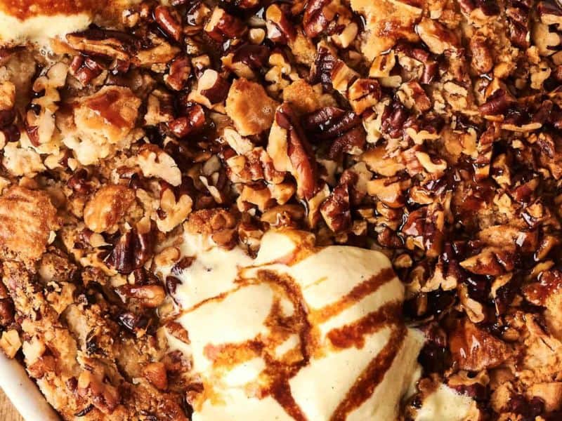 Close-up of a dessert topped with chopped pecans and a scoop of vanilla ice cream drizzled with caramel sauce.