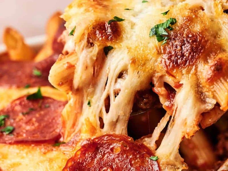 Close-up of baked pasta topped with melted, browned cheese, sliced pepperoni, and garnished with chopped parsley.