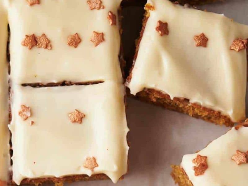 Rectangular pieces of cake with cream-colored frosting, topped with small gold star-shaped sprinkles, arranged on a white surface.