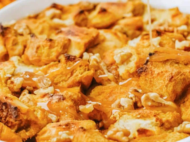 Close-up of bread pudding topped with walnuts and being drizzled with caramel sauce.