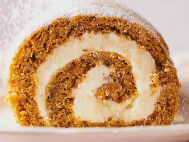Close-up of a sliced cake roll with a swirl of cream filling, dusted with powdered sugar on top.