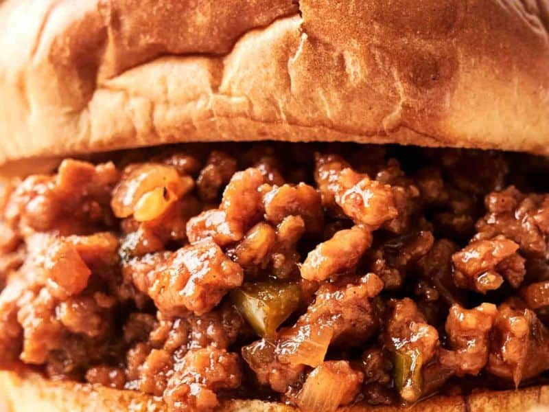 Close-up of a sloppy joe sandwich with seasoned ground meat, chopped onions, and green peppers in a toasted bun.