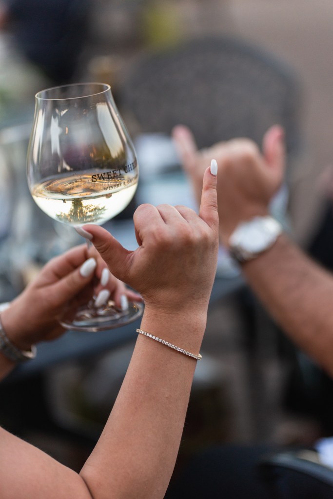 Woman's hand making "hang cool" symbol and holding wine glass in other hand