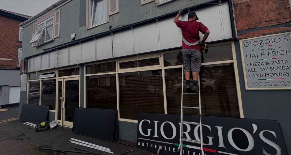 Man stood on ladder changing signage from Georgio's to Il Forno