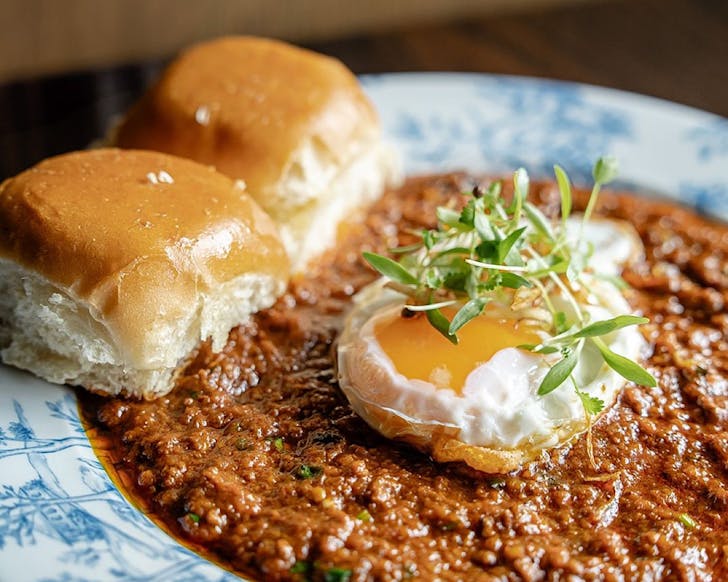 Keema Per Eedu: spicy lamb keema topped with runny fried eggs and crispy salli chips, with fresh homemade buns. 