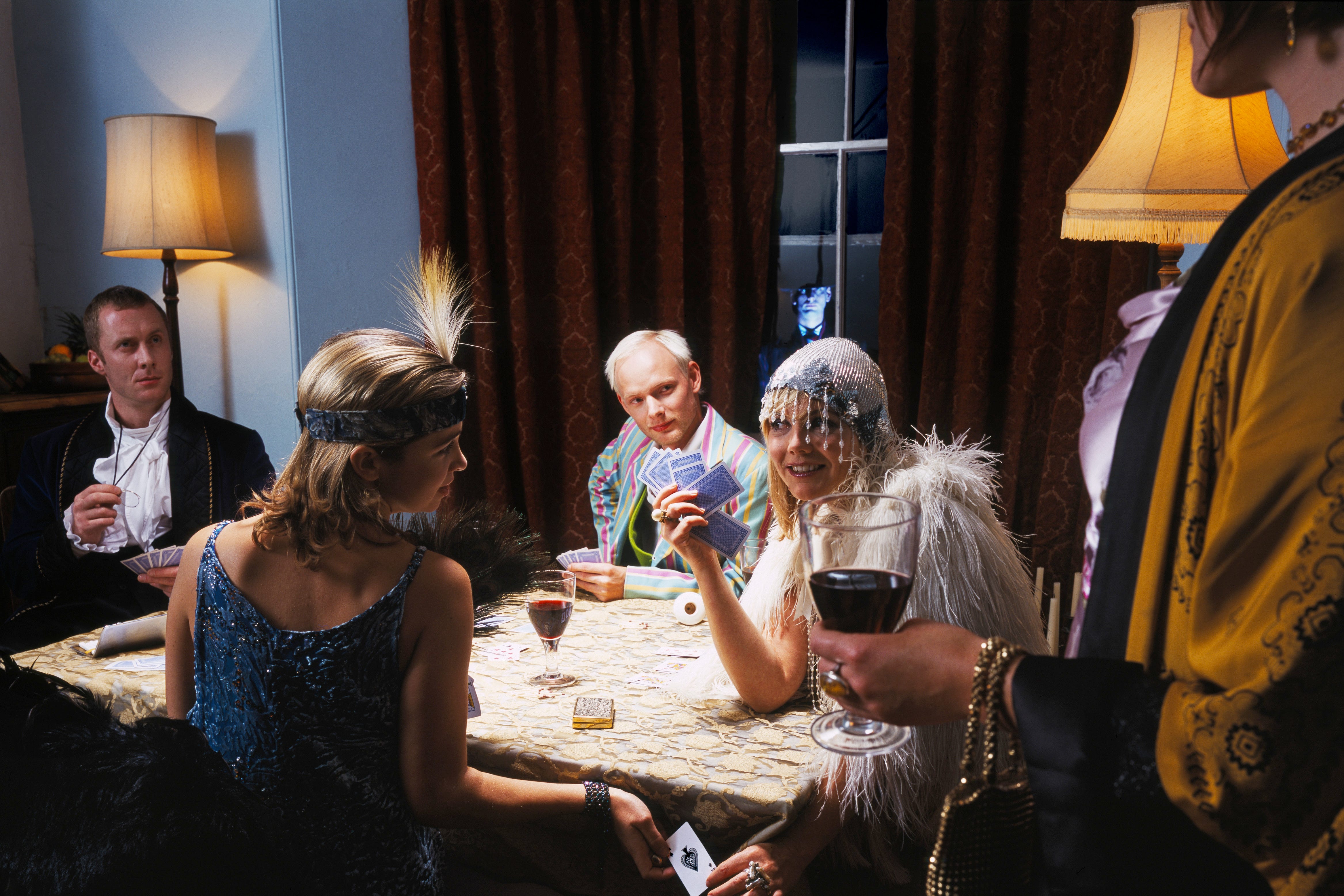 adults in fancy dress, playing cards at table, man by window outdoors
