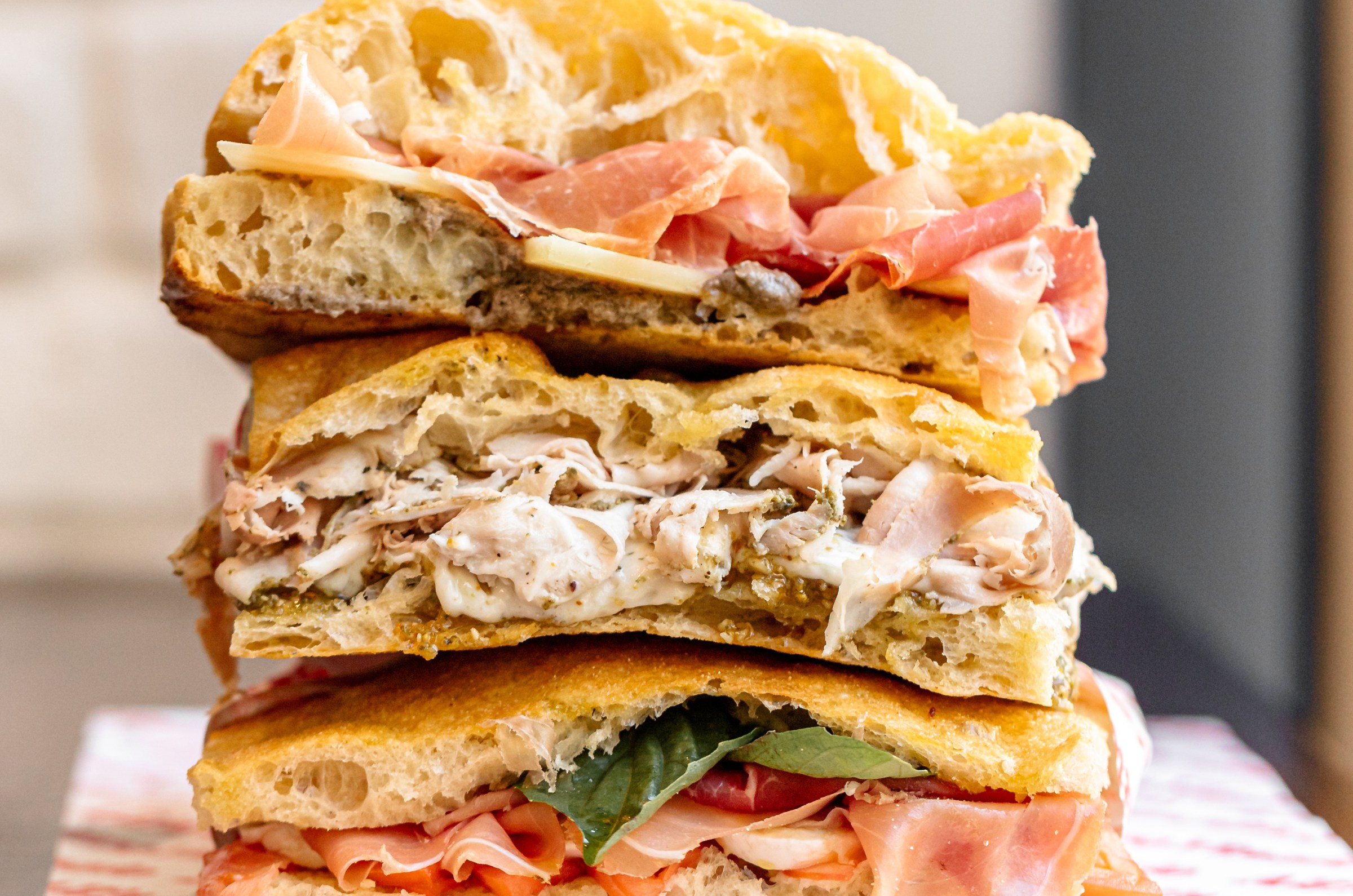 Three heaping focaccia sandwiches stacked on red and white wax paper at All’Antico Vinaio in Venice, California.