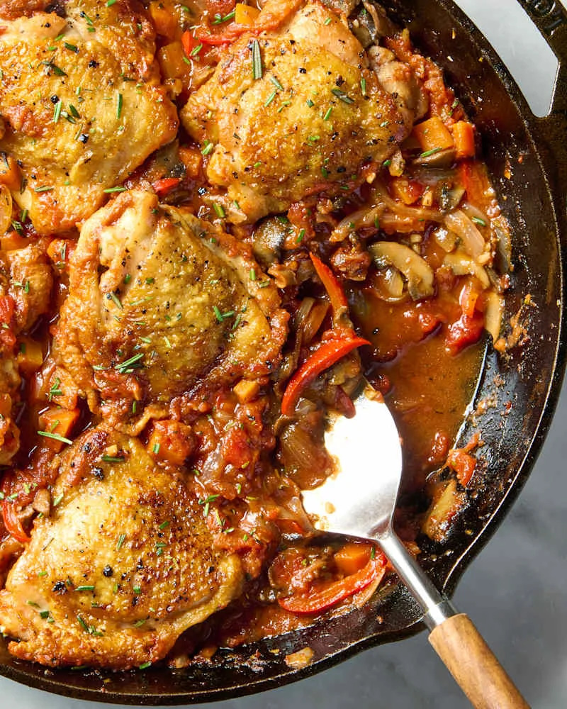 overhead shot of a skillet full of chicken cacciatore, topped with herbs