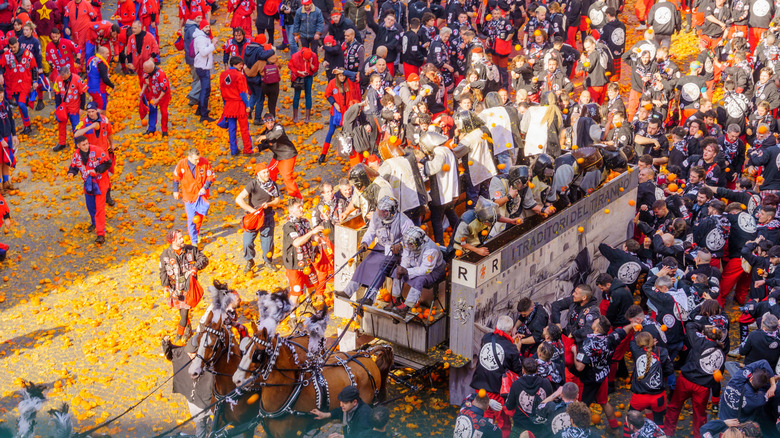 A huge crowd stands around a horse-drawn cart among smash oranges during the Battle of the Oranges event