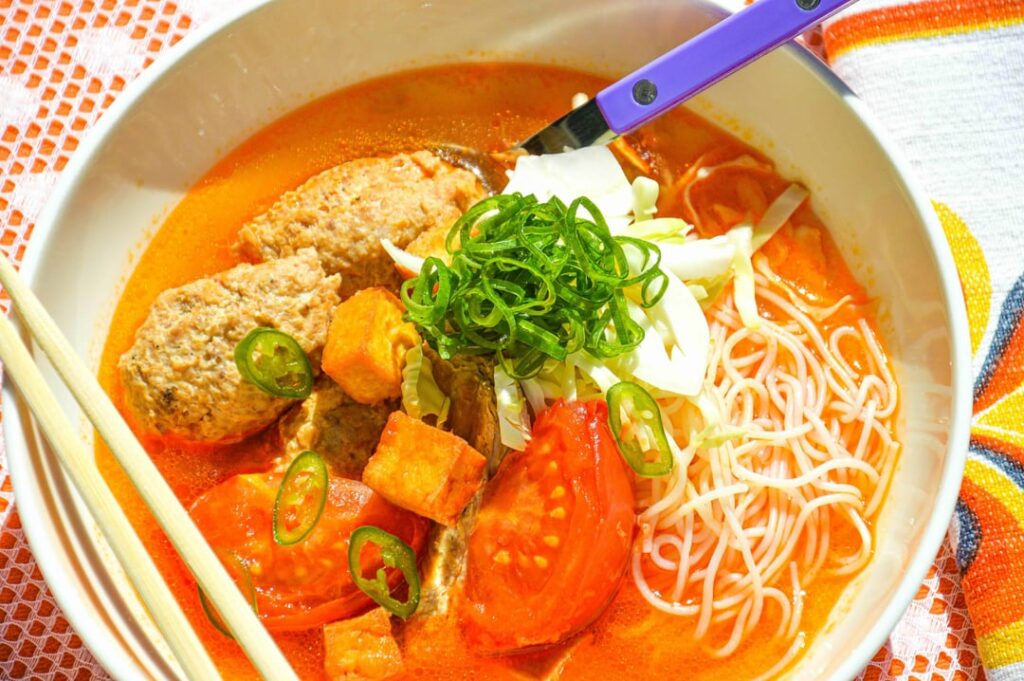 Here's bún riêu - Vietnamese tomato noodle soup featuring crab meatballs, crispy deep-fried tofu, and rice vermicelli