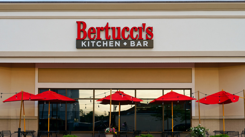 Exterior daytime photo of a Bertucci's restaurant. Five red partio umbrellas are visible.