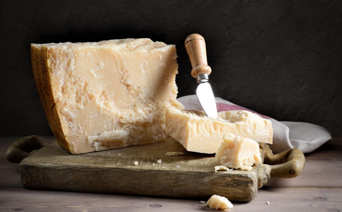 Photo shows a large block of parmesan cheese on a chopping board with a knife and towel