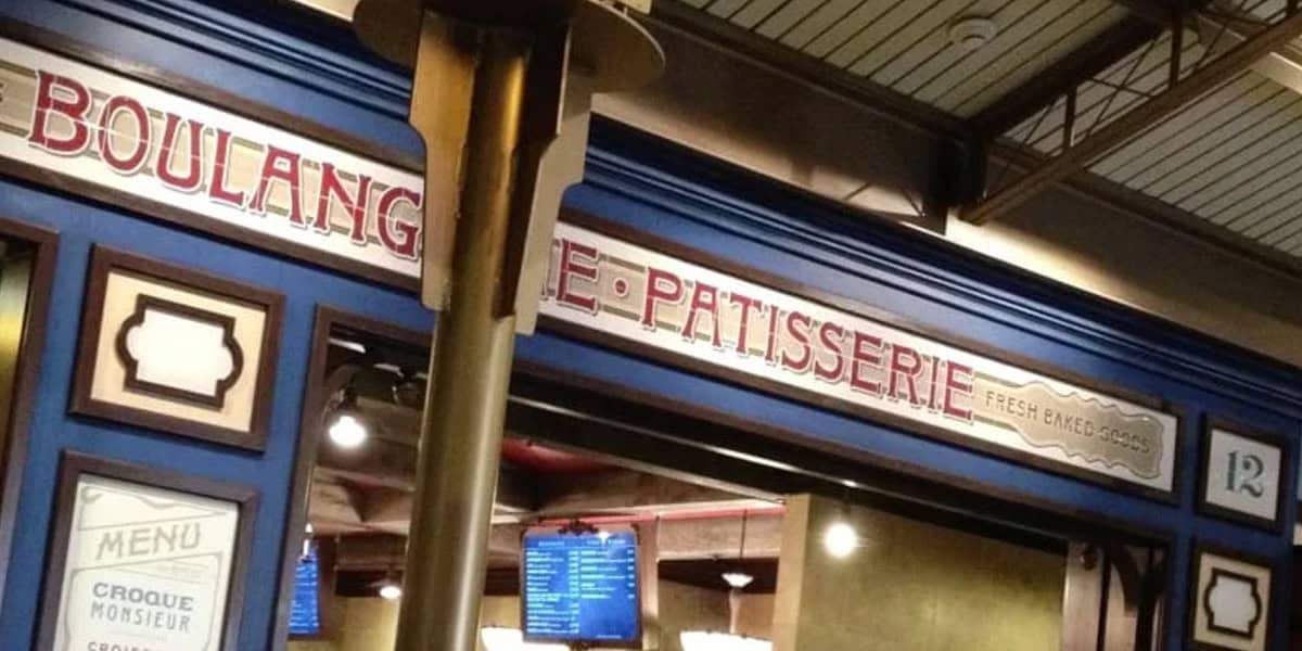 A bakery storefront with a blue facade and a sign that reads "BOULANGERIE - PATISSERIE." Menu boards and a digital screen are visible inside, evoking the charm of Les Halles Boulangerie-Patisserie.