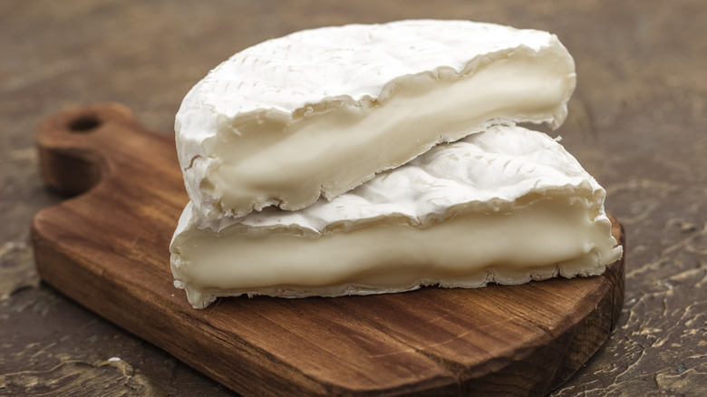 A wheel of brie cut in halves on a wooden board