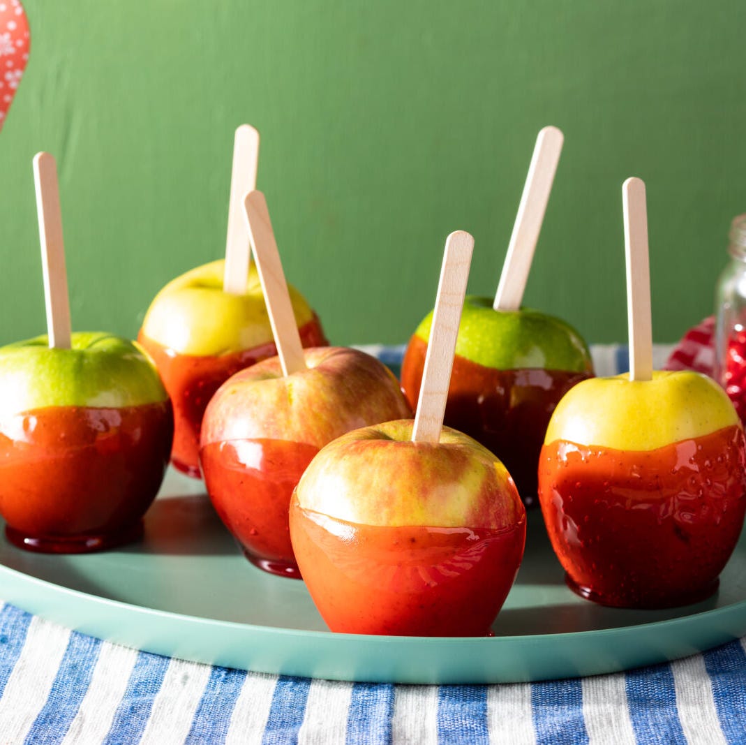 candied apples coated with red cinnamon candy with popsicle sticks on blue striped linen with cinnamon candy in the background