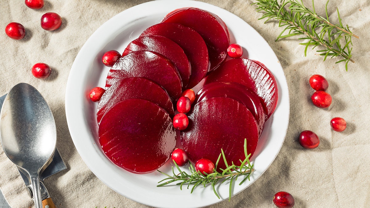 Canned cranberry jauice on plate surrounded by garnishes on holiday table including cranberries.