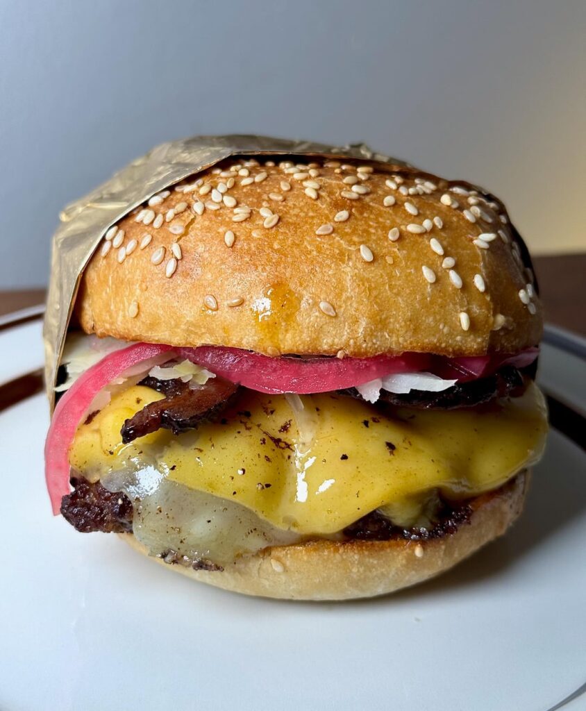 1/3lb slight-smash with Pepper Jack, American, Black Forest bacon, Jamaican jerk mayo, fresh kraut, pickled red onions.