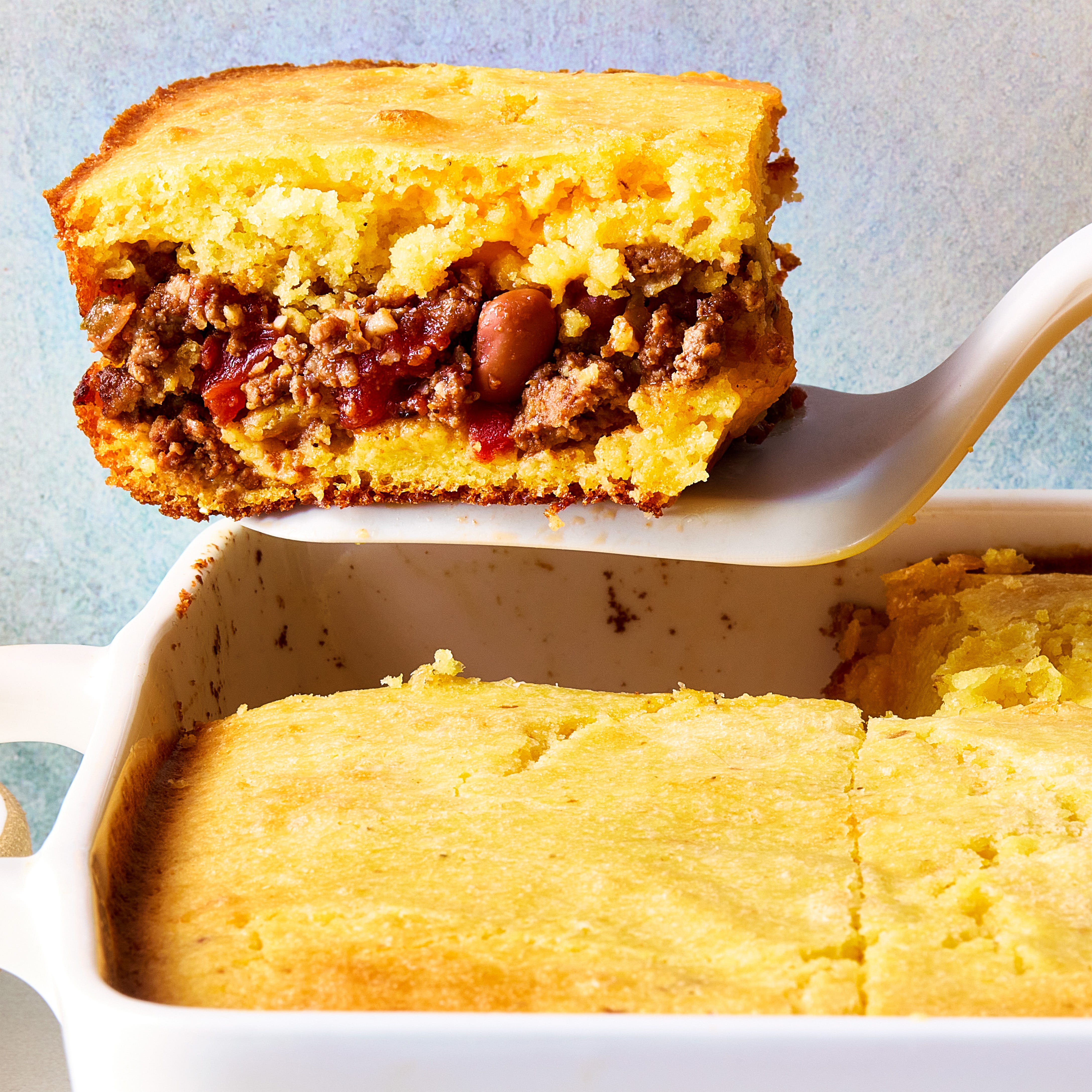 cornbread in a casserole dish with a layer of chili in the middle