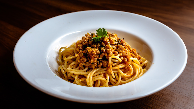 white bowl of spaghetti topped with meat sauce