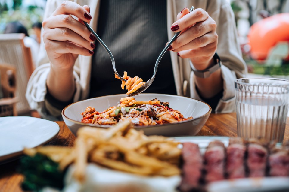 A person twirling spaghetti bolognese with a fork and spoon at a dining table.
