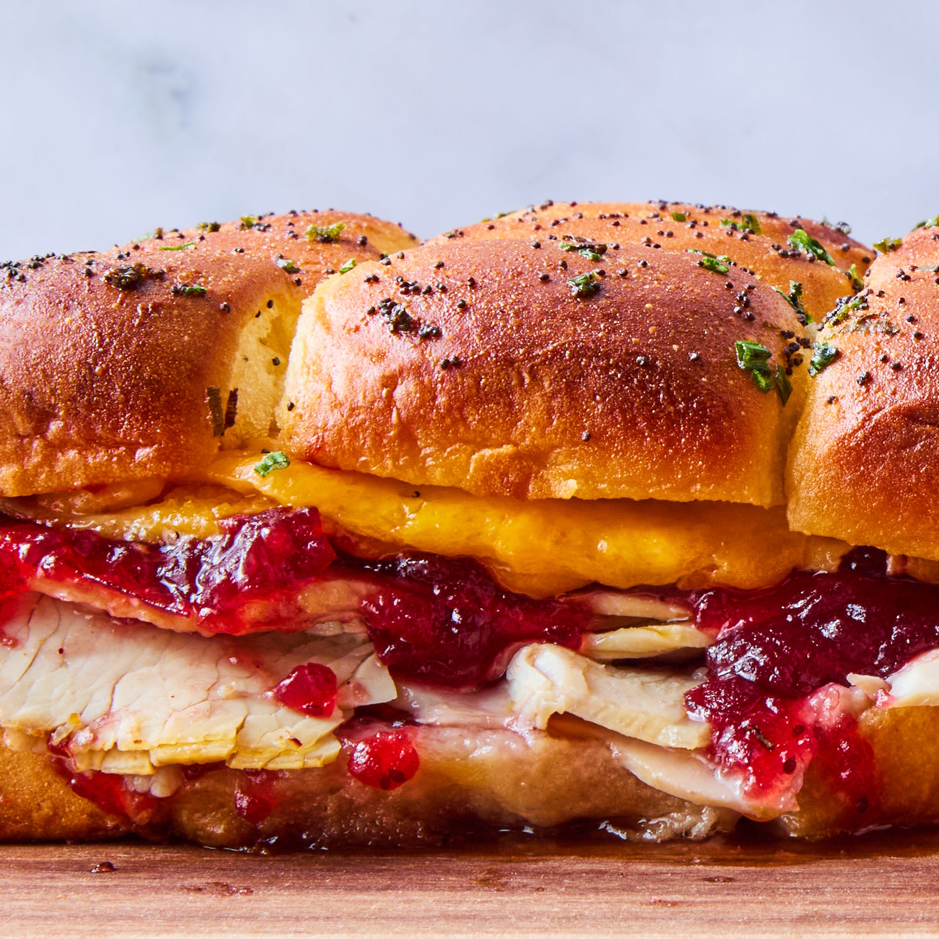 sliders filled with sliced turkey, cranberry sauce, and cheese topped with a poppyseed butter topping
