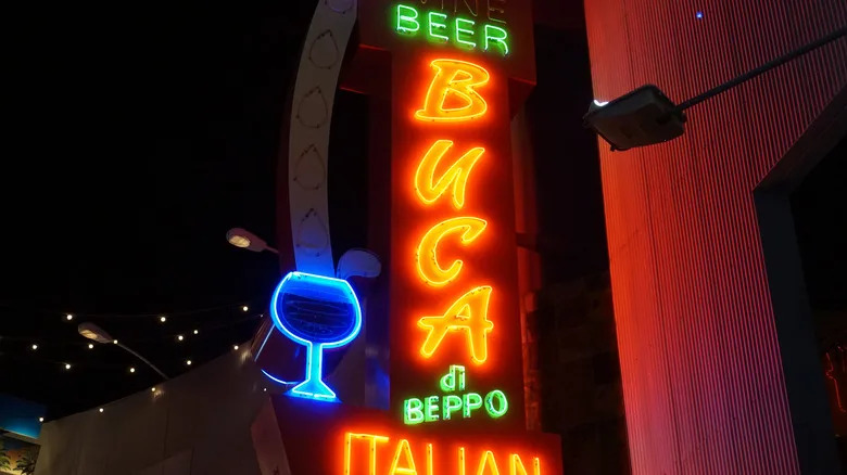 A neon Buca di Beppo sign is lit on the side of a restaurant.
