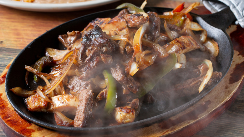 Skillet of sizzling fajitas with onions and peppers.