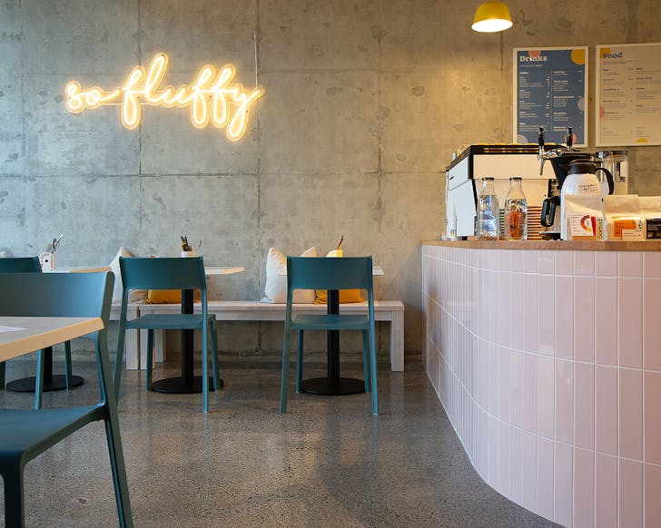 The interior of the gorgeous Fluff cafe in Grafton shows a neon sign saying So Fluffy and a pastel interior.