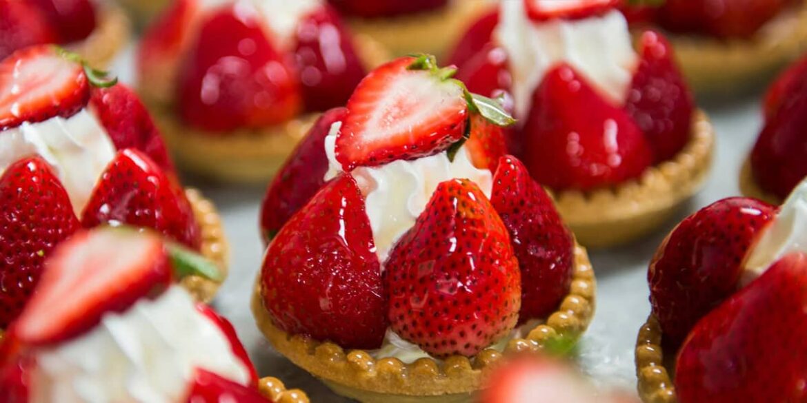 Close-up of strawberry tarts from Les Halles Boulangerie-Patisserie, featuring fresh strawberries, whipped cream, and a golden pastry base, all arranged closely together on a tray.