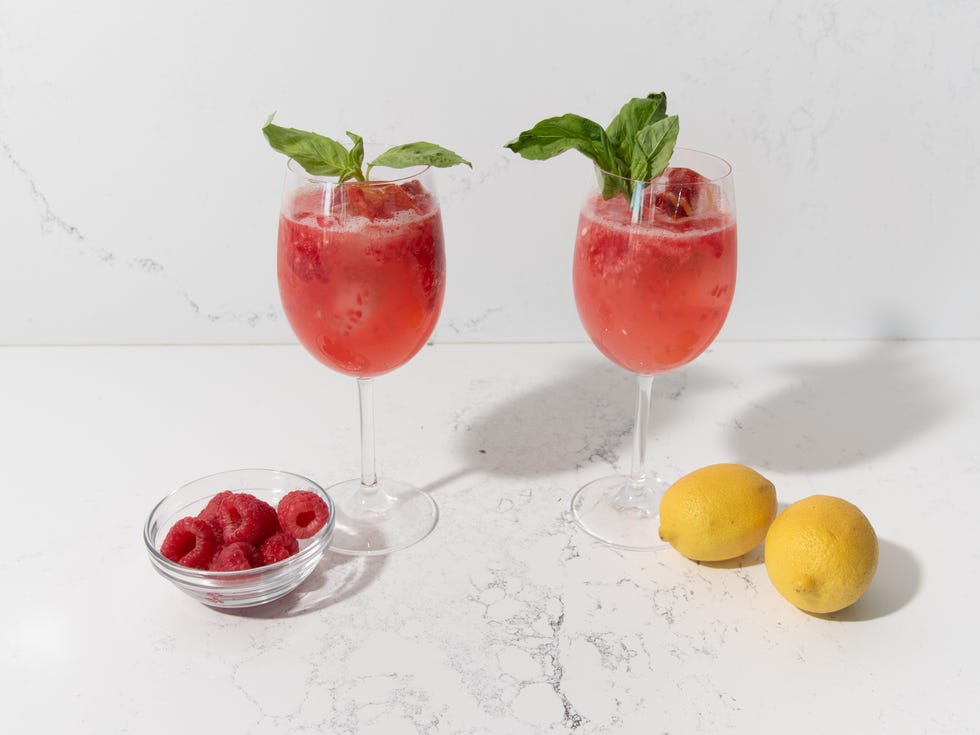 meghan markle sparkling raspberry lemonade in 2 wine glasses with a bowl of raspberries and a halved lemon