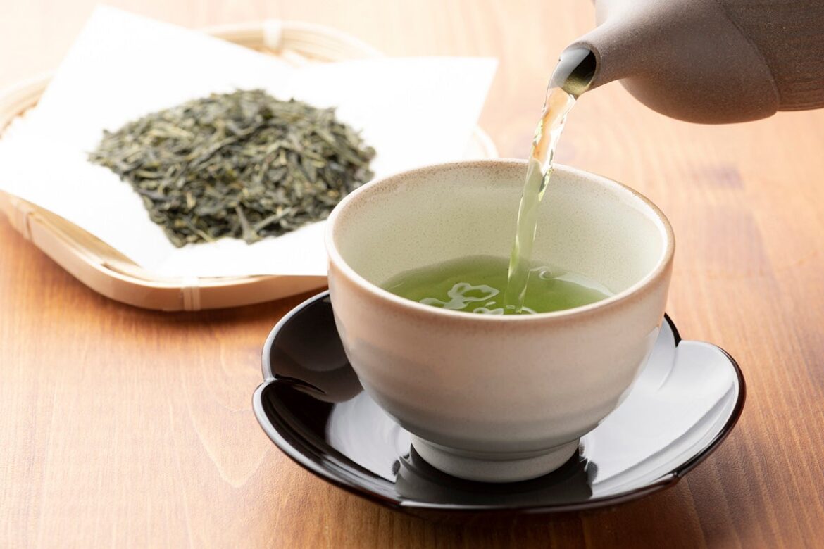 Green tea is poured from a teapot into a cup.