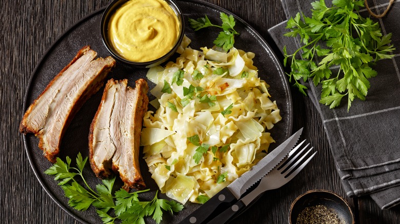 black plate with haluski, meat, and sauce accented with herbs on the side