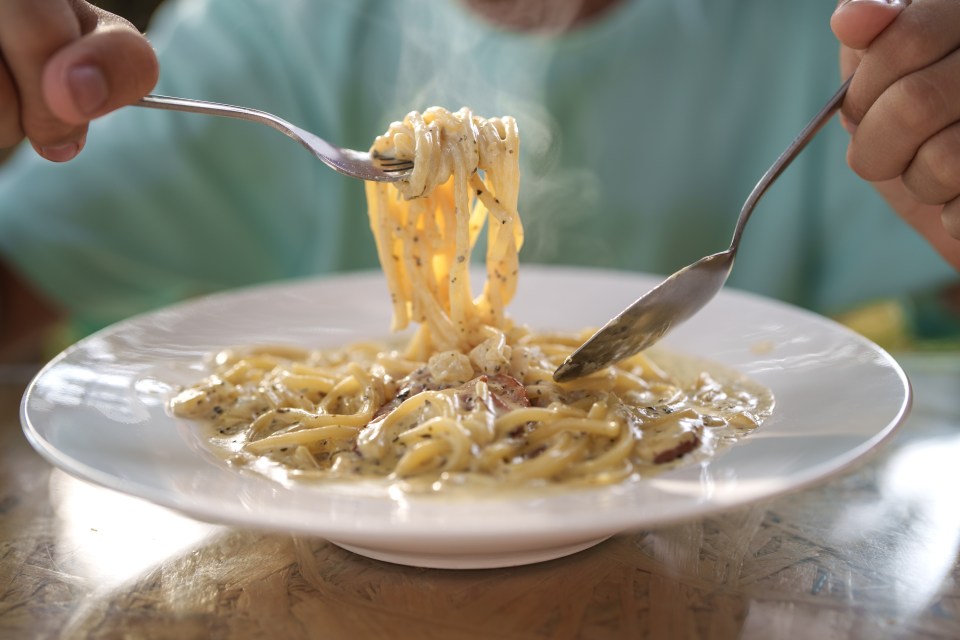 Person twirling creamy carbonara pasta with a fork.