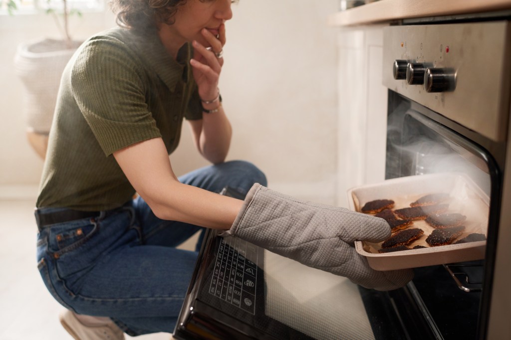 Woman taking burnt cookies from oven.