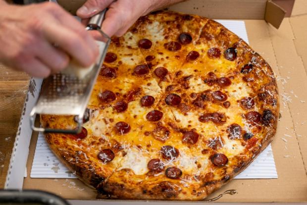 Chef Alex Figura grates mimolette cheese onto a pepperoni pizza at Redeemer Pizza's second pop-up of the winter, which sold out in three minutes, inside Good Bread Denver on Saturday, Jan. 30, 2021.