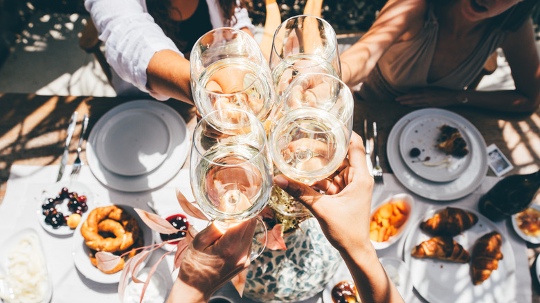people clinking wine glasses over a table with food