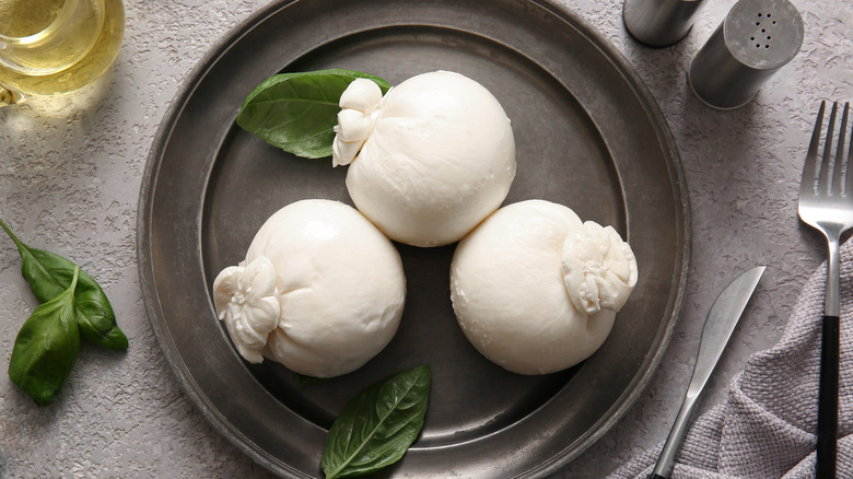 three balls of burrata on a gray plate with basil leaves