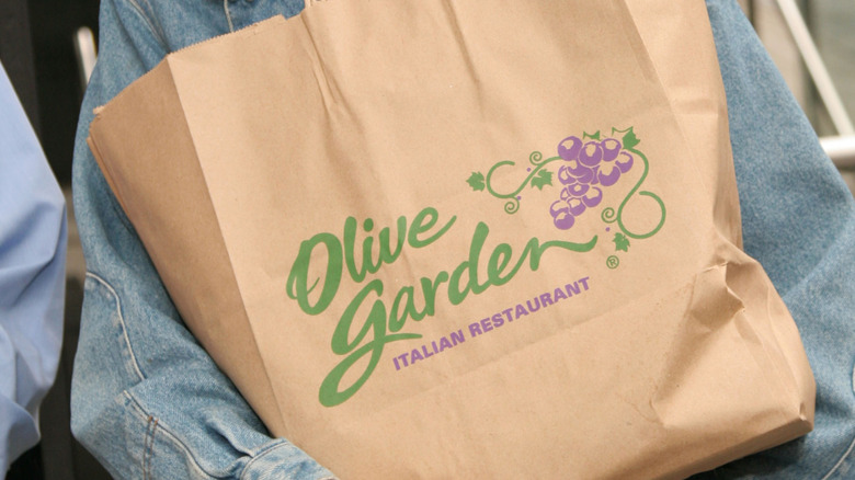 A takeout bag of Olive Garden food, carried by a person in a denim jacket