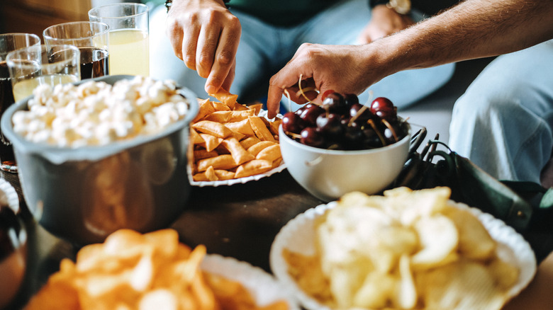 People's hands reach for various snacks in bowls.